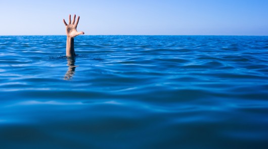 Help needed. Drowning man's hand in sea or ocean.